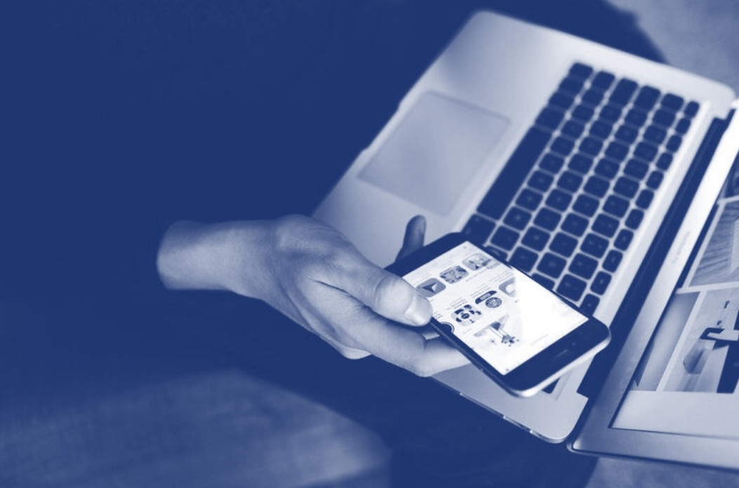 a person is holding a cell phone in front of a laptop .