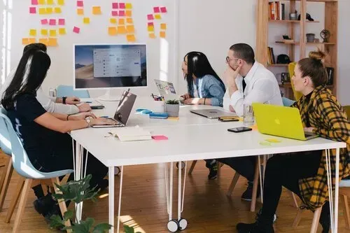 A group of people are sitting around a table with laptops.
