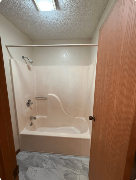Small bathroom with a white walk-in shower and built-in bench behind an open wood door.