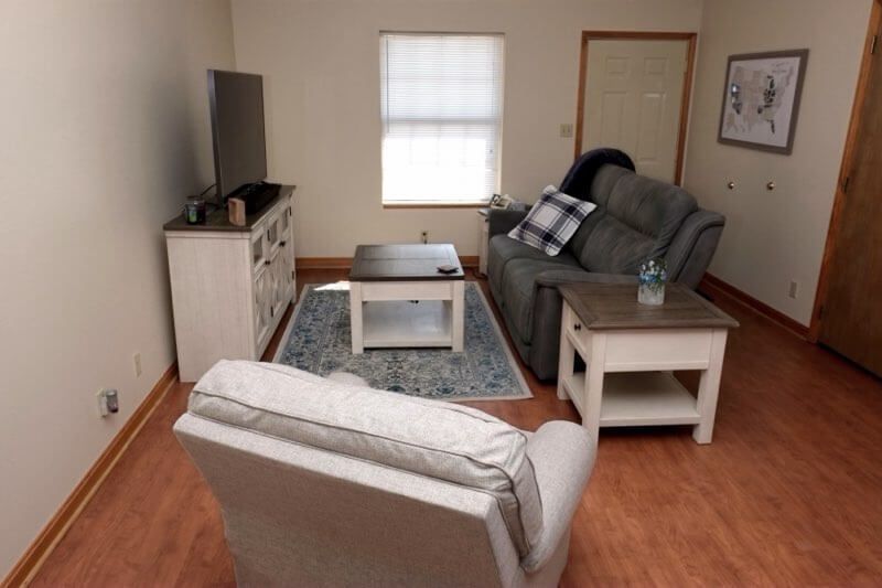 Small living room with gray sofa, armchair, TV, coffee table, and hardwood floors