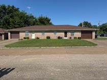 Single-story brick building with a brown roof, small windows, and a grassy lawn in front