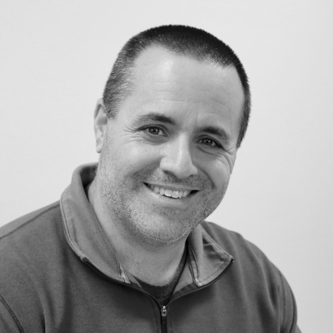 A man with a beard is smiling in a black and white photo.