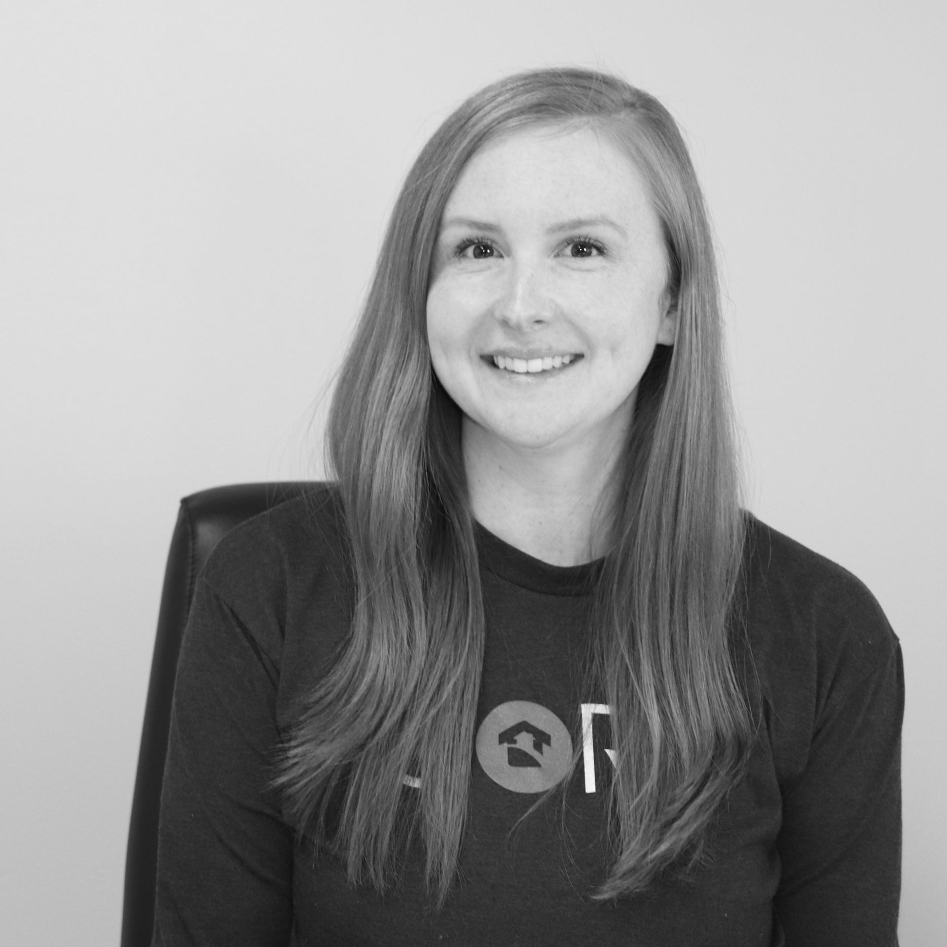 A woman is smiling in a black and white photo while sitting in a chair.