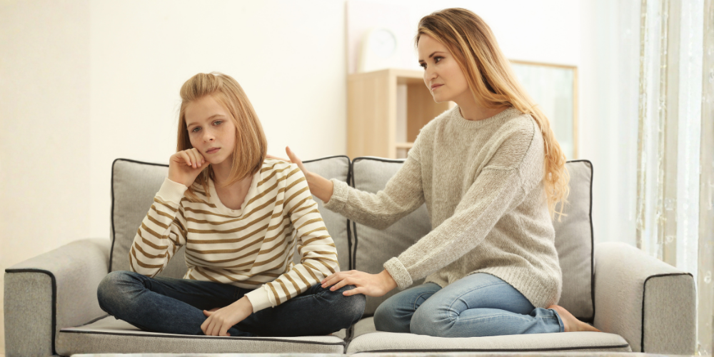 Two women sitting on a couch, one comforting the other in a bright living room
