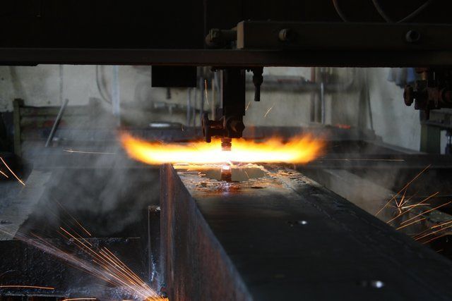 In una fabbrica, una macchina industriale taglia il metallo, producendo scintille arancioni brillanti e fumo.