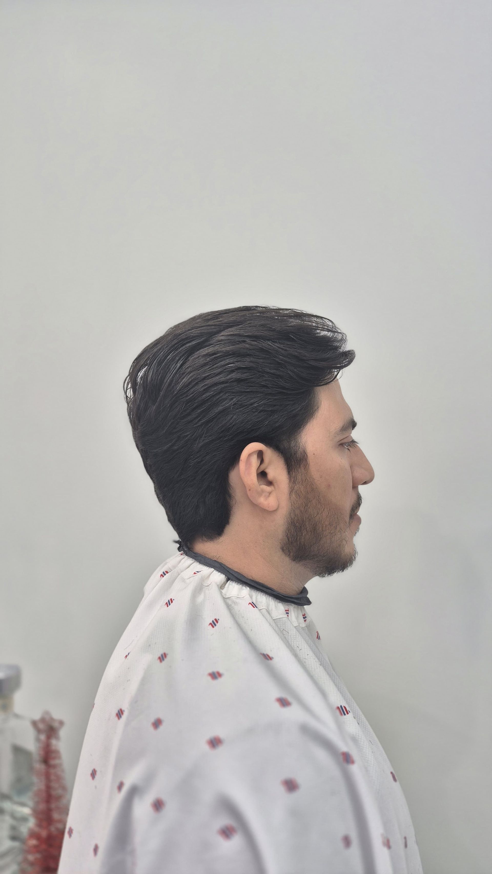 Man in barber cape with wavy hair and beard profile.