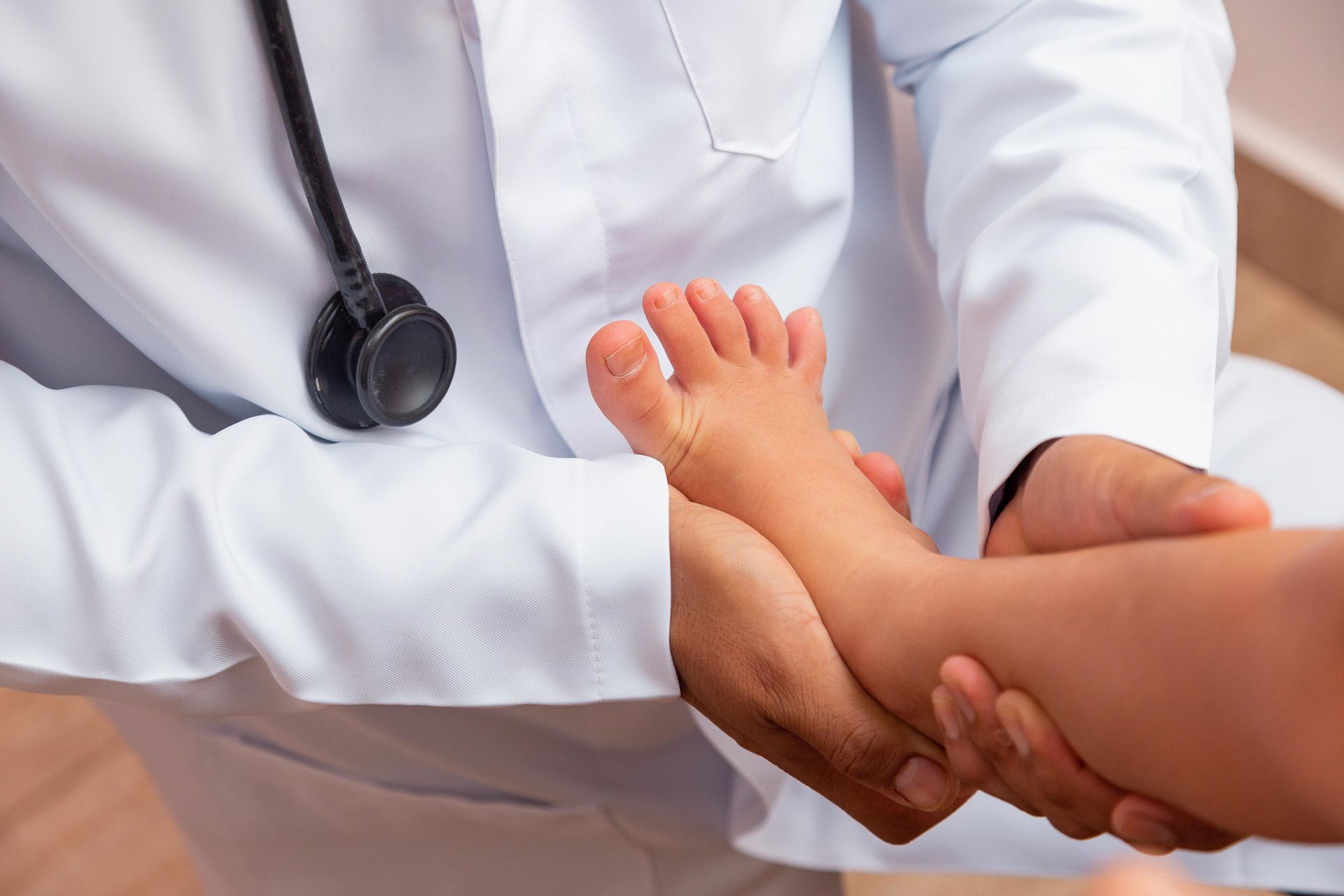Doctor examining a child's foot in a clinic; the doctor wears a white coat, stethoscope.