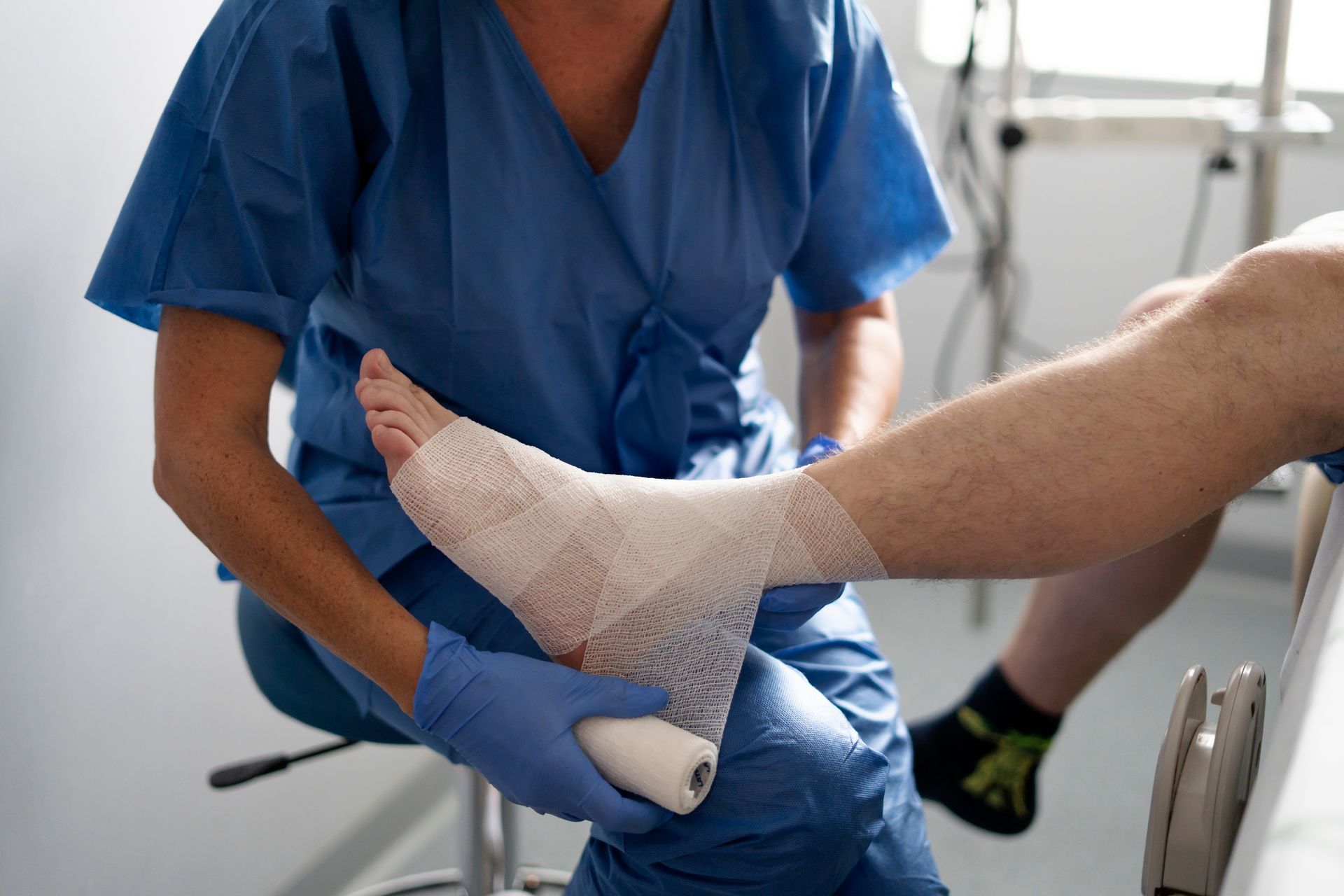 Nurse wrapping a patient's foot with a bandage in a medical setting.