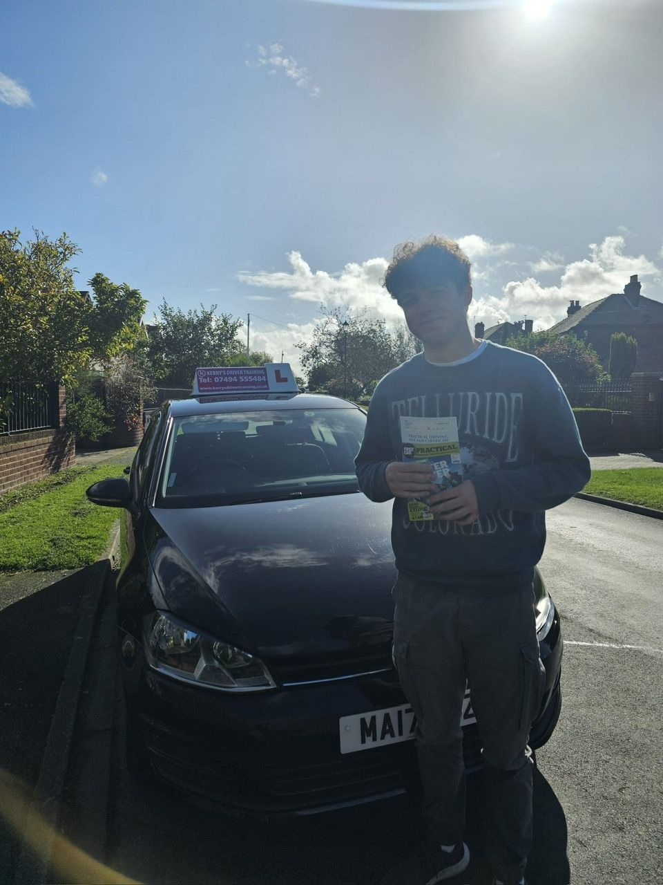 A young person stands smiling next to a black car with a