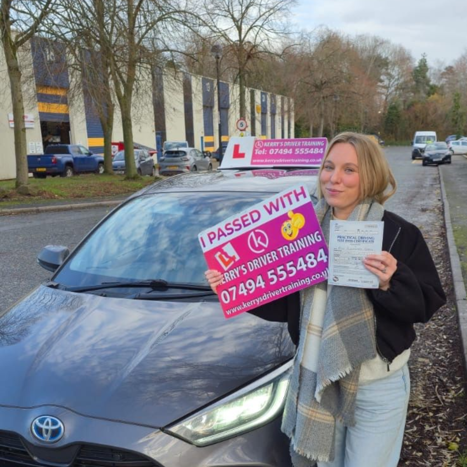Woman with a driver's license next to a gray Toyota Yaris, holding a