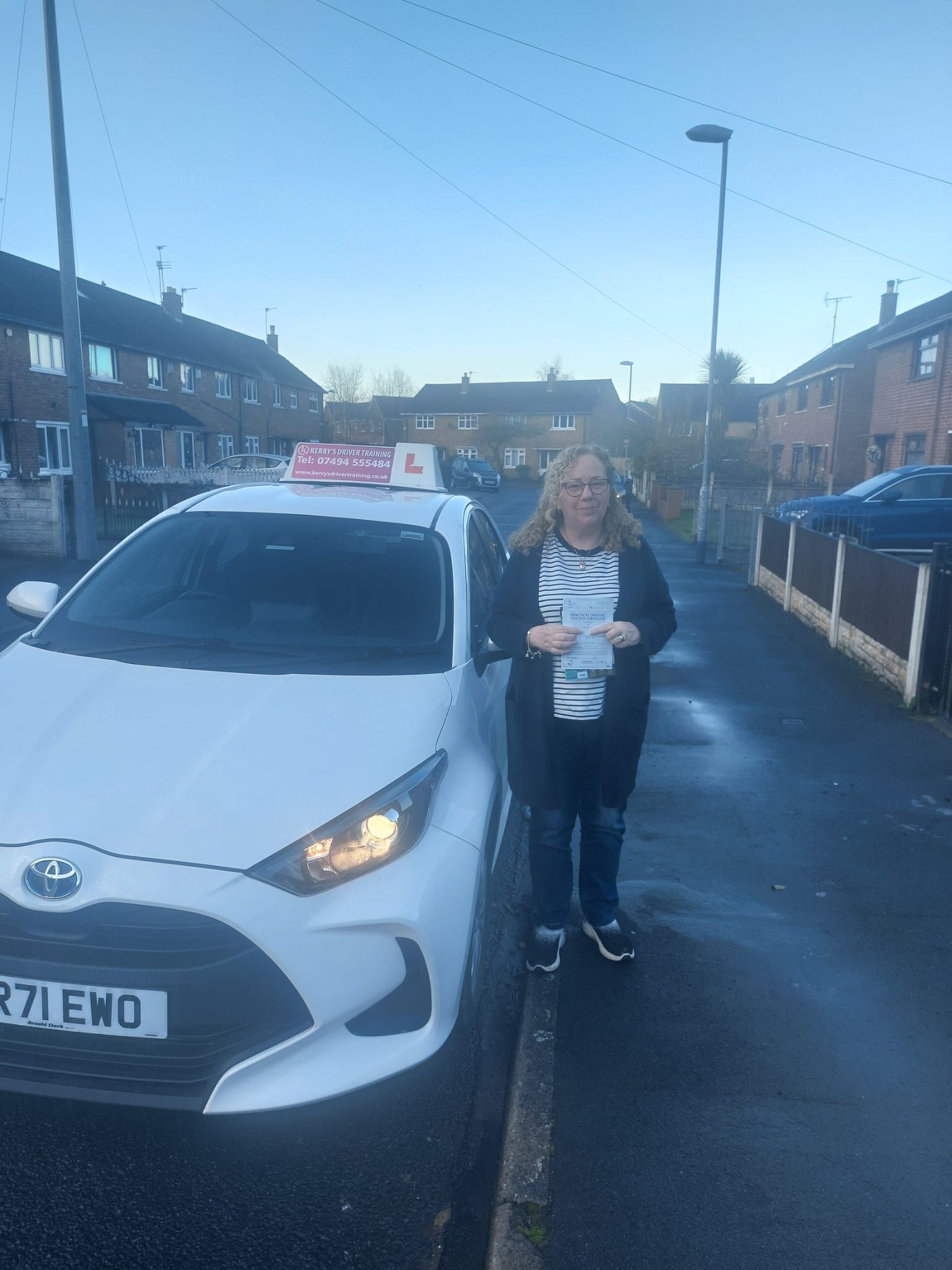 A woman is standing next to a white car on the side of the road.