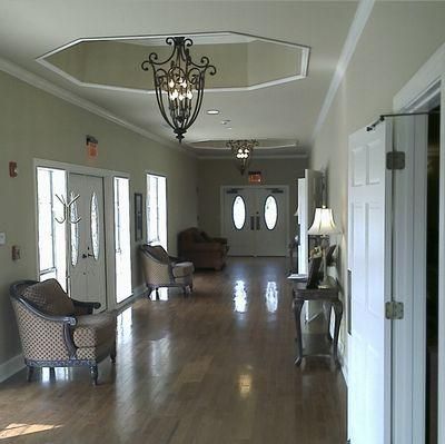 Bright lobby hallway with hardwood floors, chairs, chandeliers, and double doors at the end