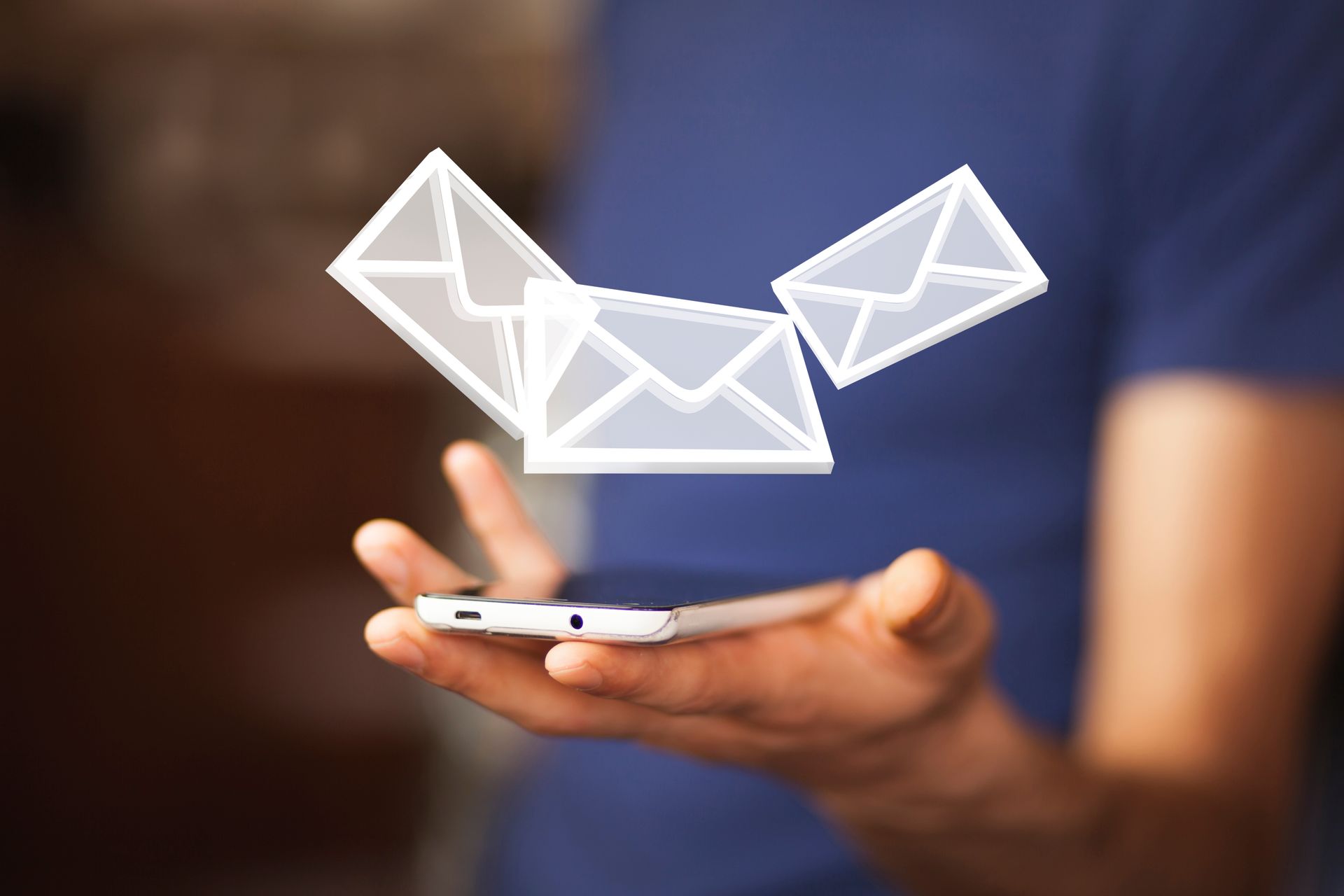 A person is holding a cell phone with envelopes coming out of it.