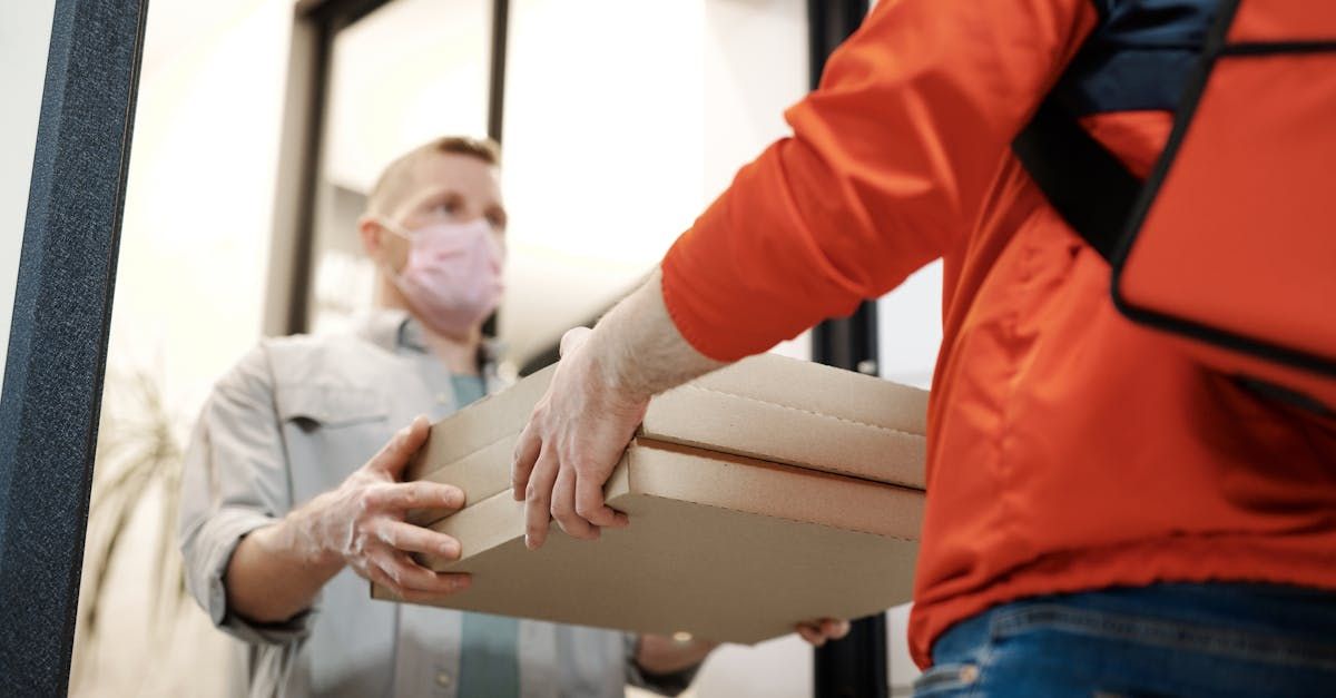 A delivery man wearing a mask and gloves is handing a box to a customer.