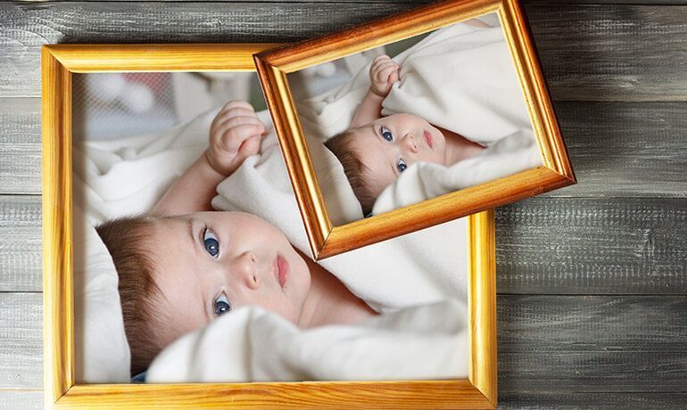 Two overlapping gold frames with close-up photos of a baby on a gray wooden surface