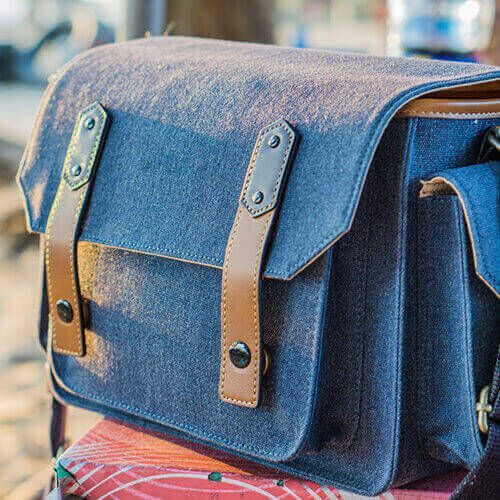 Blue denim satchel bag with tan leather straps on a colorful surface