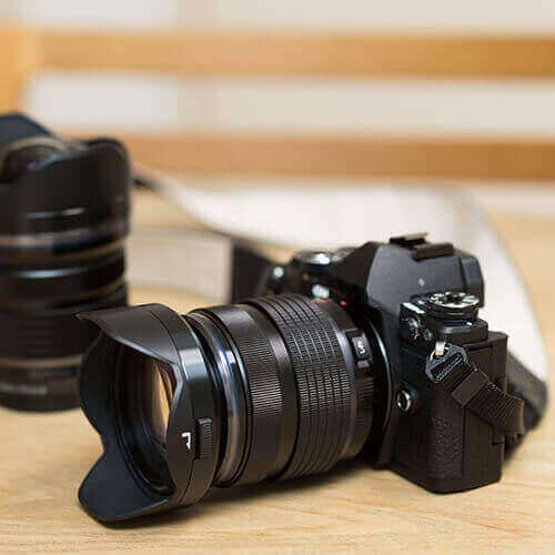 Camera with a zoom lens and lens hood on a wooden table, with another lens blurred in the background