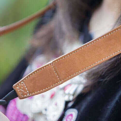 Brown leather shoulder strap over a blurred black garment with a white-and-pink pattern