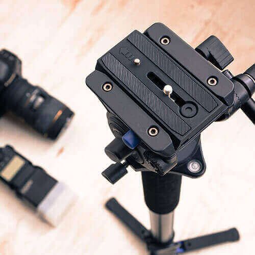 Black tripod head with quick-release plate on a tripod, viewed from above.