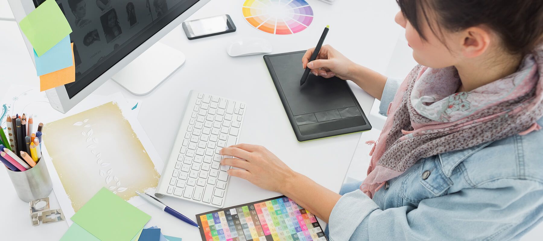Child drawing at a desk with a graphics tablet, color swatches, and art supplies.