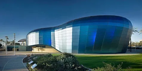 Striking modern exterior of Aquarium of the Pacific under a clear blue sky, with sunlight reflecting off its curved blue walls