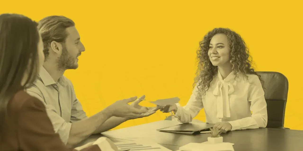 Three colleagues smiling at a table, reviewing documents together against a bright yellow background