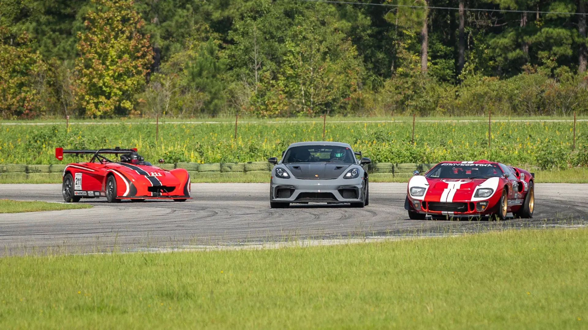 Three sports cars are racing on a track with trees in the background