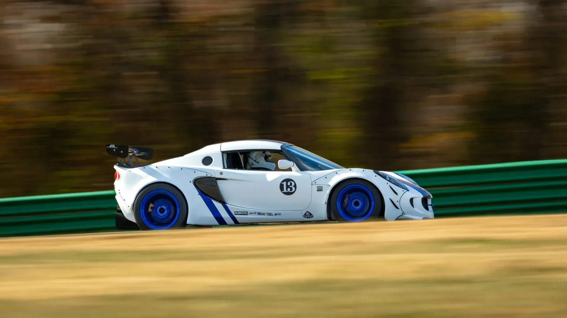 A white race car with blue wheels is driving on a track