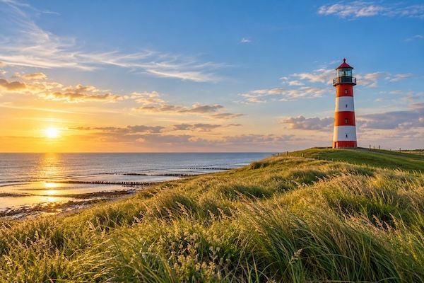 Illustratives Küstenmotiv für Ostfriesland mit Leuchtturm, Dünengras und Meer im Abendlicht