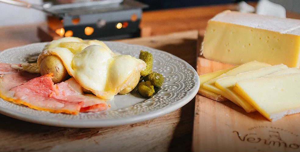 Um prato de comida com queijo e batatas em uma mesa de madeira.