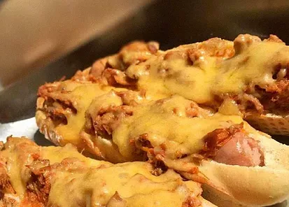 Um close de um cachorro-quente coberto de queijo em um pão.
