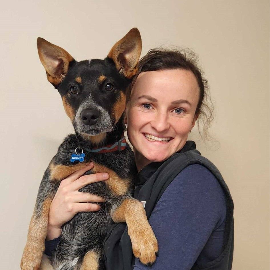 Woman holding a black-and-tan dog, both facing the camera and smiling