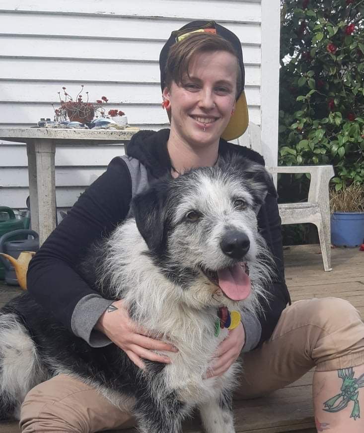 Person smiling and hugging a shaggy black-and-white dog outdoors on a porch