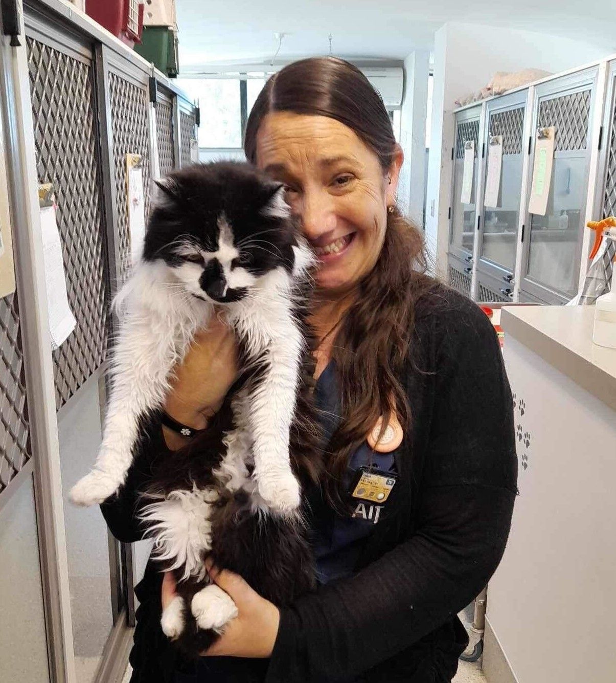 Woman smiling while holding a black-and-white cat in a hallway lined with cages
