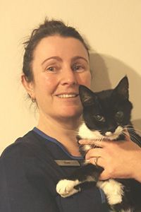 Woman holding a black-and-white cat against a plain wall