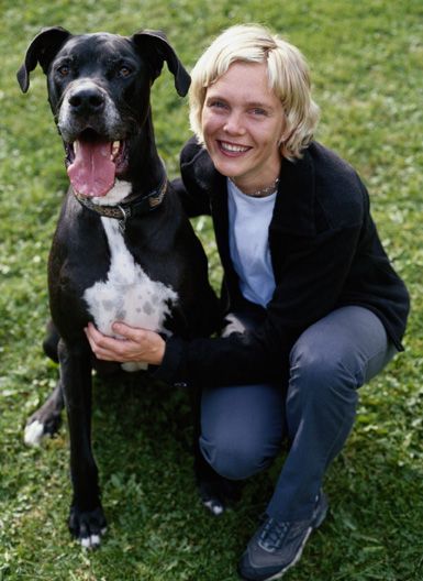 Woman kneeling beside a black-and-white dog on grass, both looking at the camera and smiling