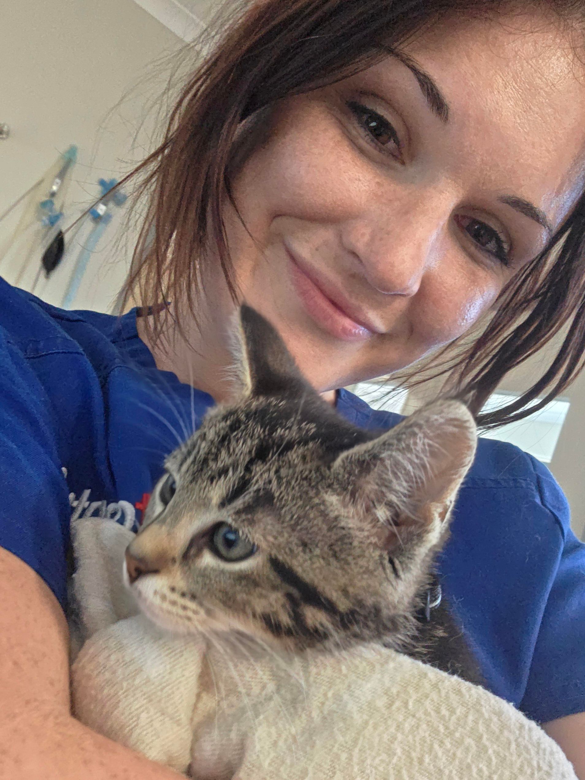 Woman holding a gray tabby kitten and smiling indoors