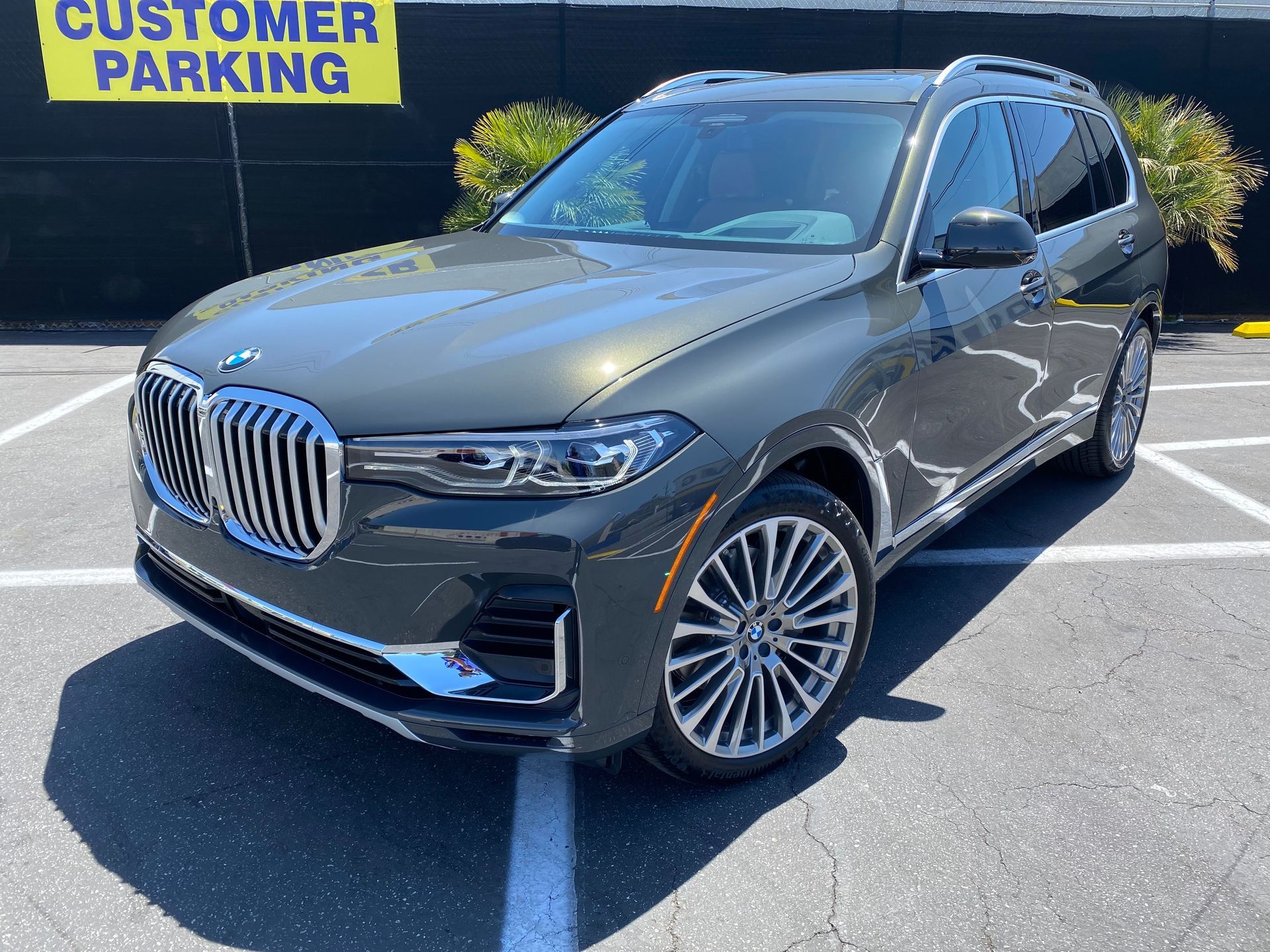 A bmw x7 is parked in a parking lot next to a customer parking sign.