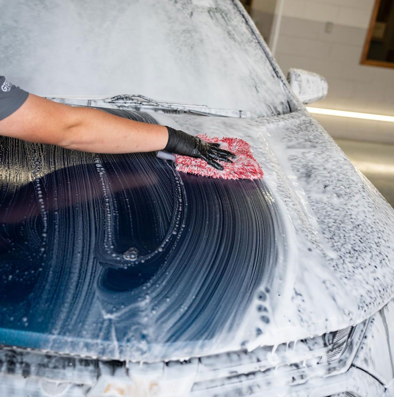 A man is washing a car with a brush in a garage.