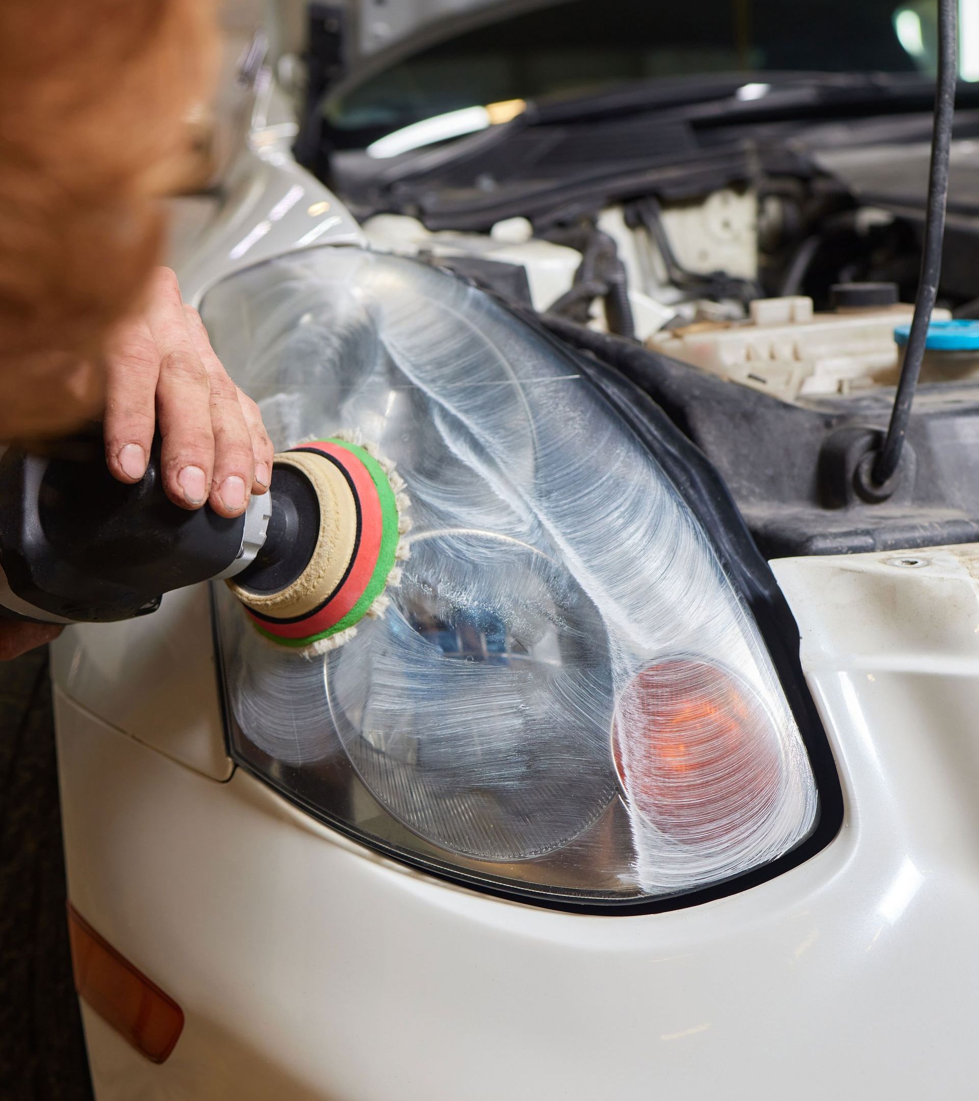 A person is polishing a car headlight with a polisher.