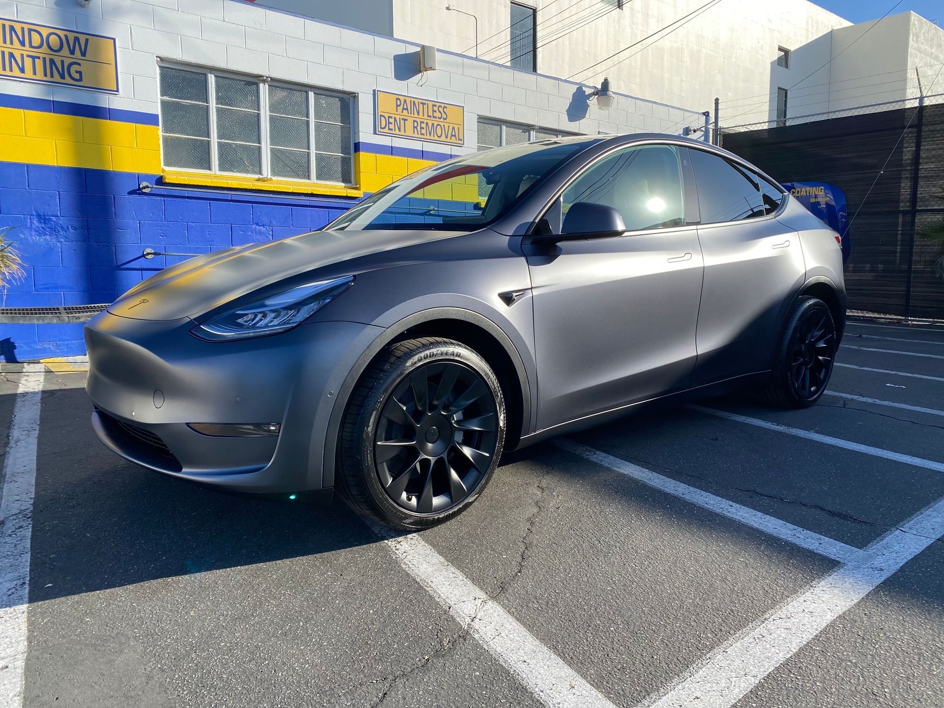 A tesla model y is parked in a parking lot in front of a building.
