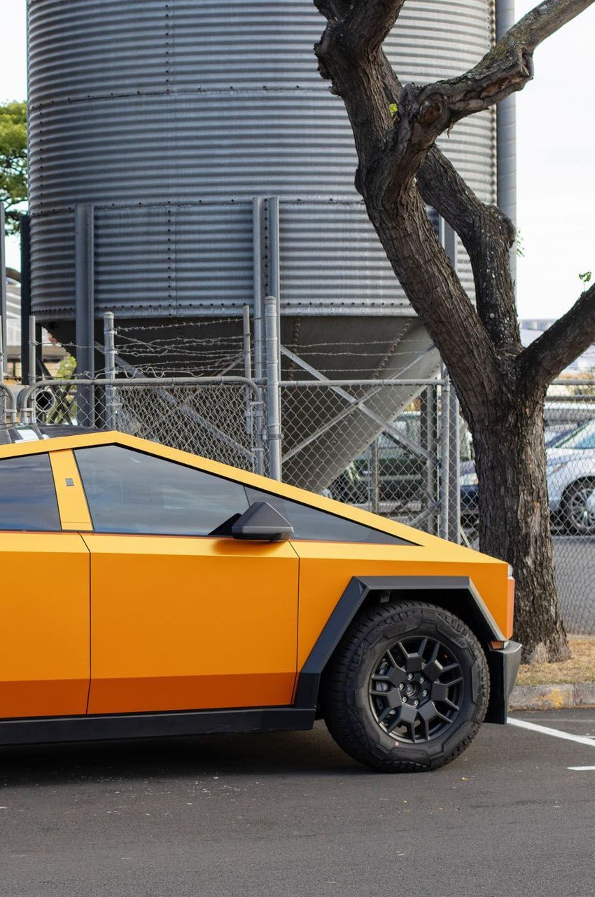 A yellow car is parked next to a tree in front of a silo