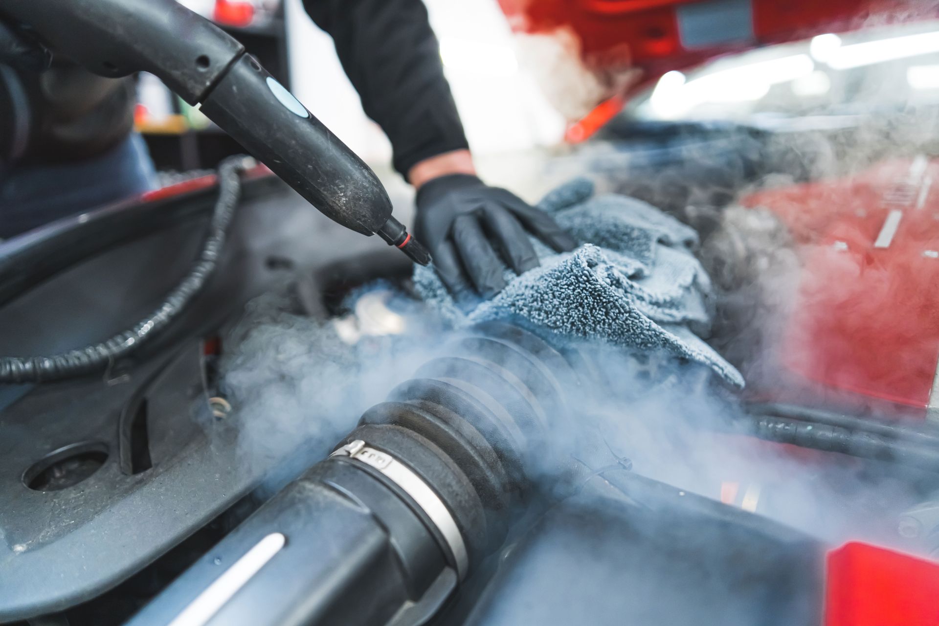 A person is cleaning the engine of a car with a steam cleaner.