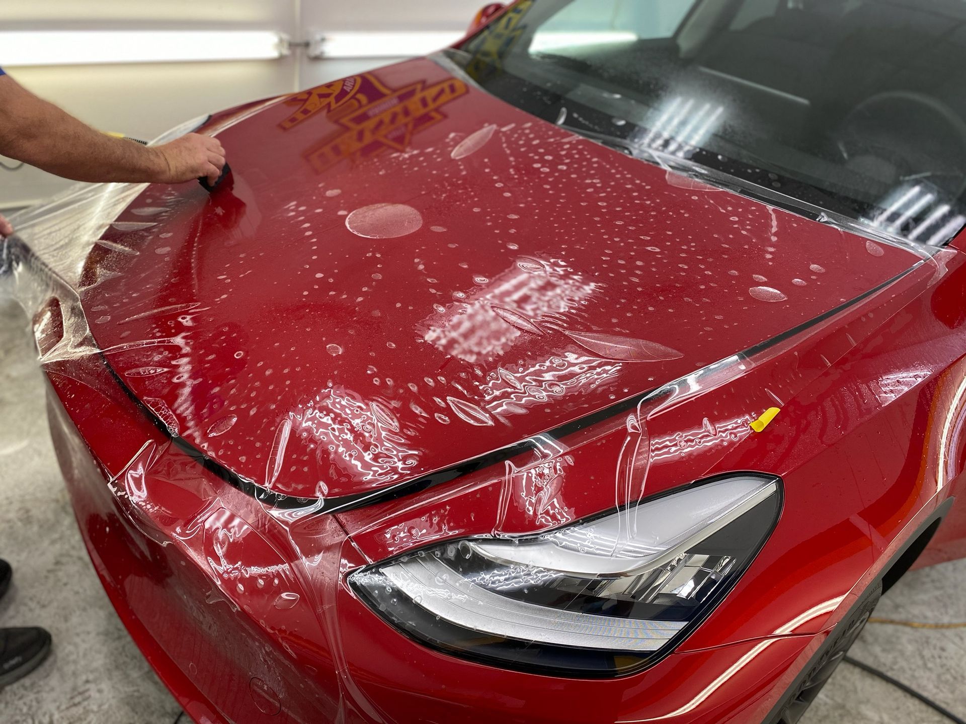 A man is covering the hood of a red tesla model 3.