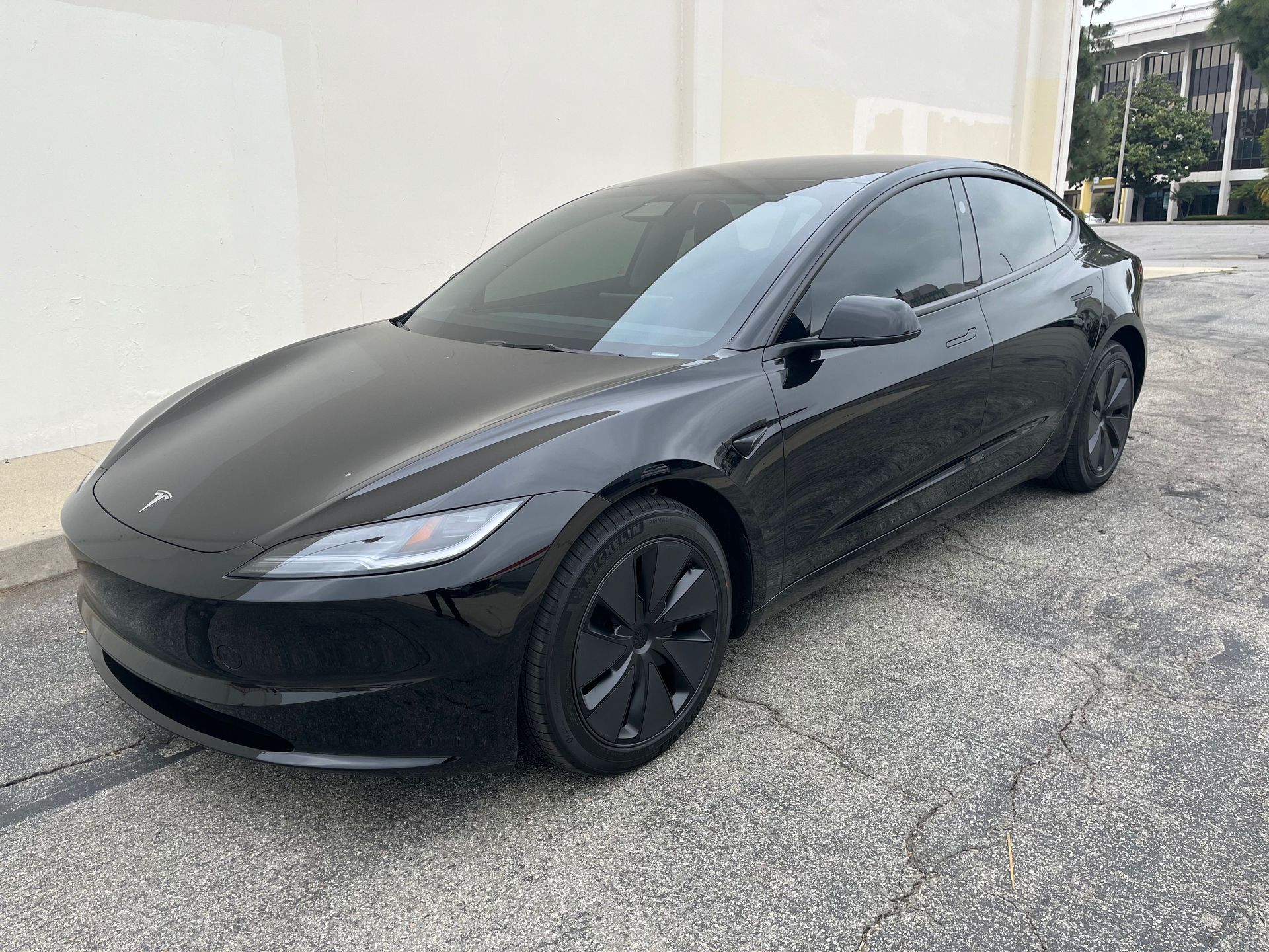 A black tesla model 3 is parked in front of a building.