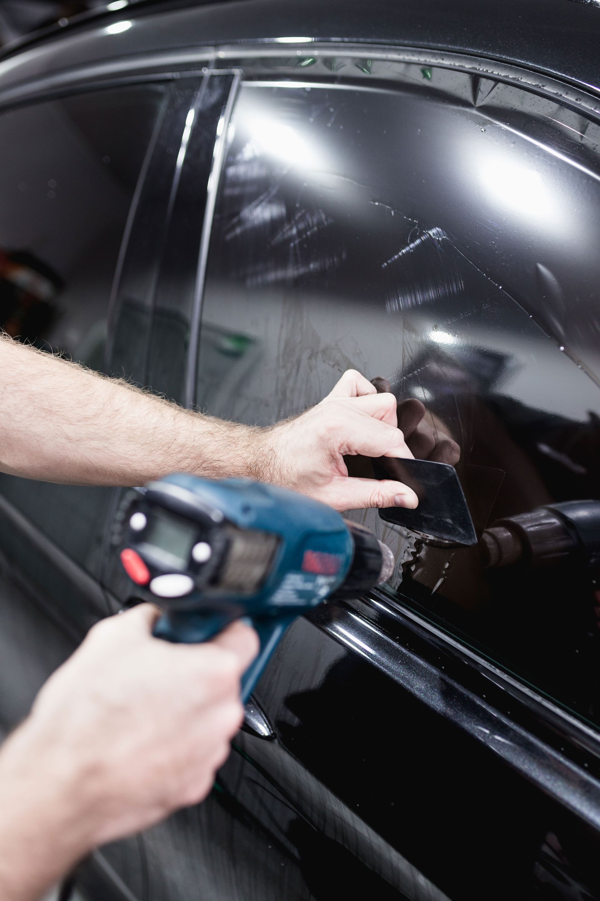 A person wearing black gloves is cleaning a car window.