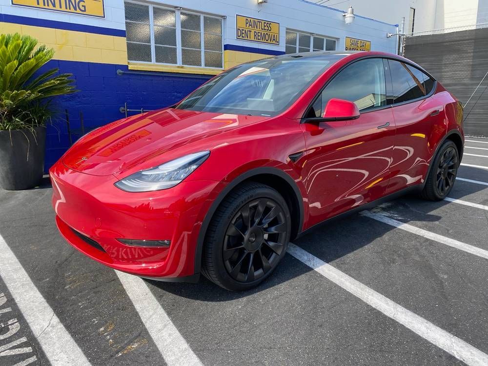 A red tesla model y is parked in a parking lot in front of a building.