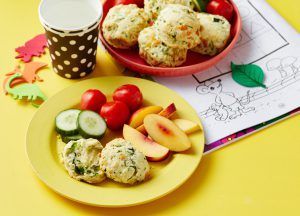 A child's lunch with savory veggie bites, cucumber slices, cherry tomatoes, and peach slices on a yellow plate and bowl.