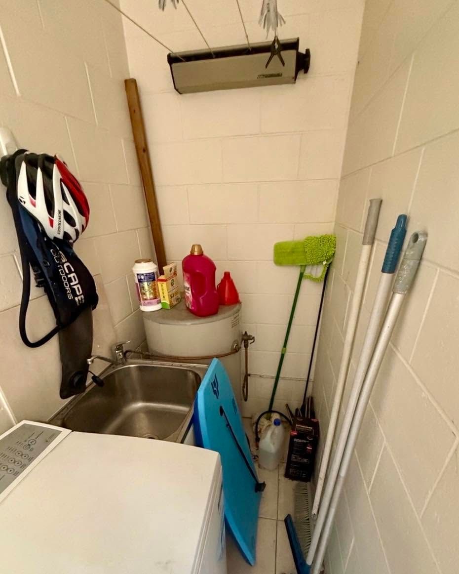 Utility closet with sink, cleaning tools, helmets, mop, broom, and buckets in a tiled room