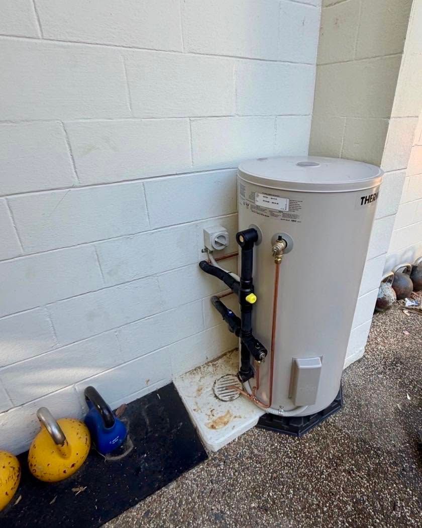 Outdoor utility tank beside a white wall, with yellow propane cylinders on the ground nearby.